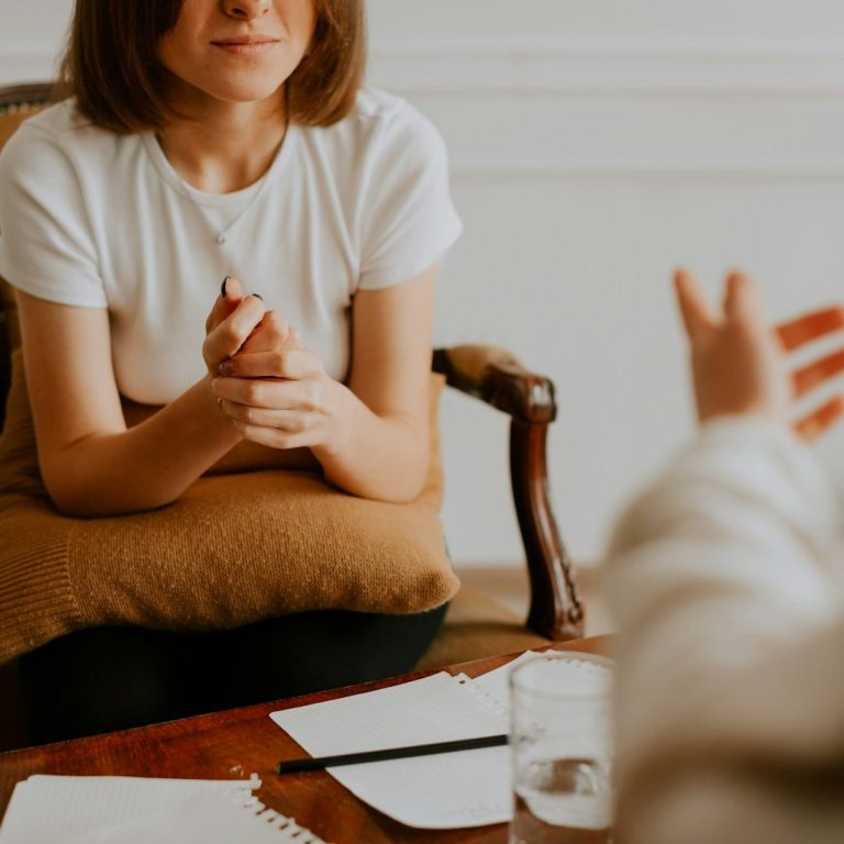 consult Zelfinzicht Een vrouw in een witte shirt zit op een stoel, luisterend naar een gesprekspartner.