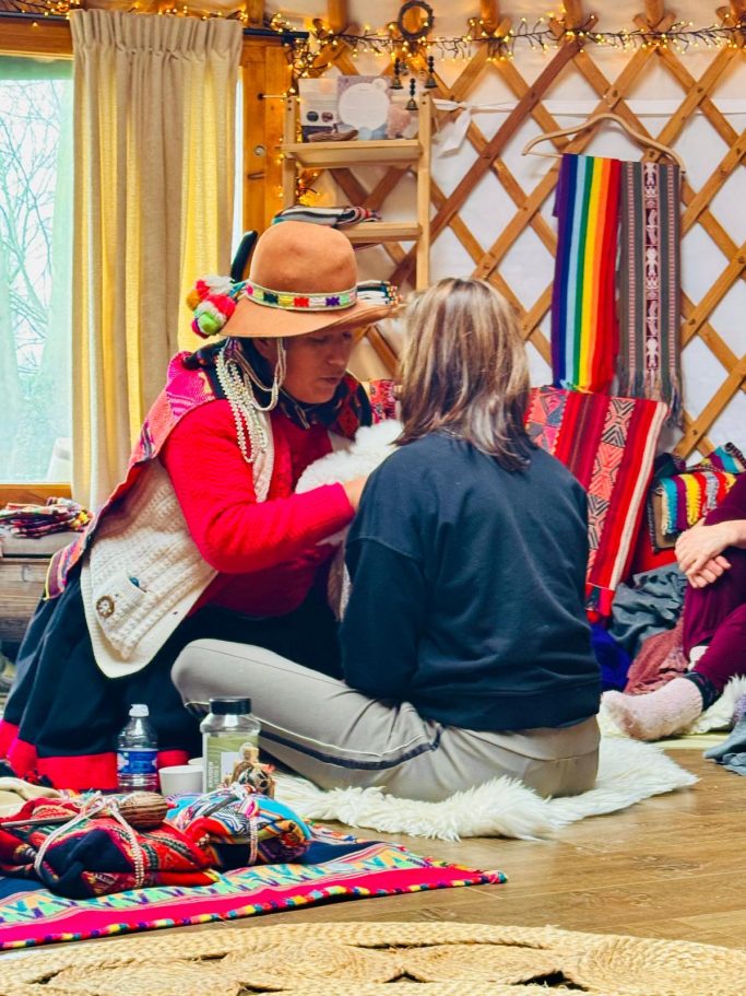 Person in traditional clothing engaging in a healing ceremony, surrounded by colorful textiles.